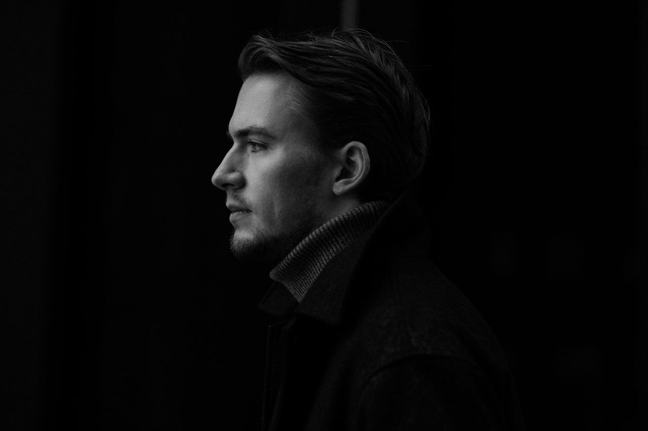 A striking black and white side profile portrait of a fashionable young man in stylish outerwear.